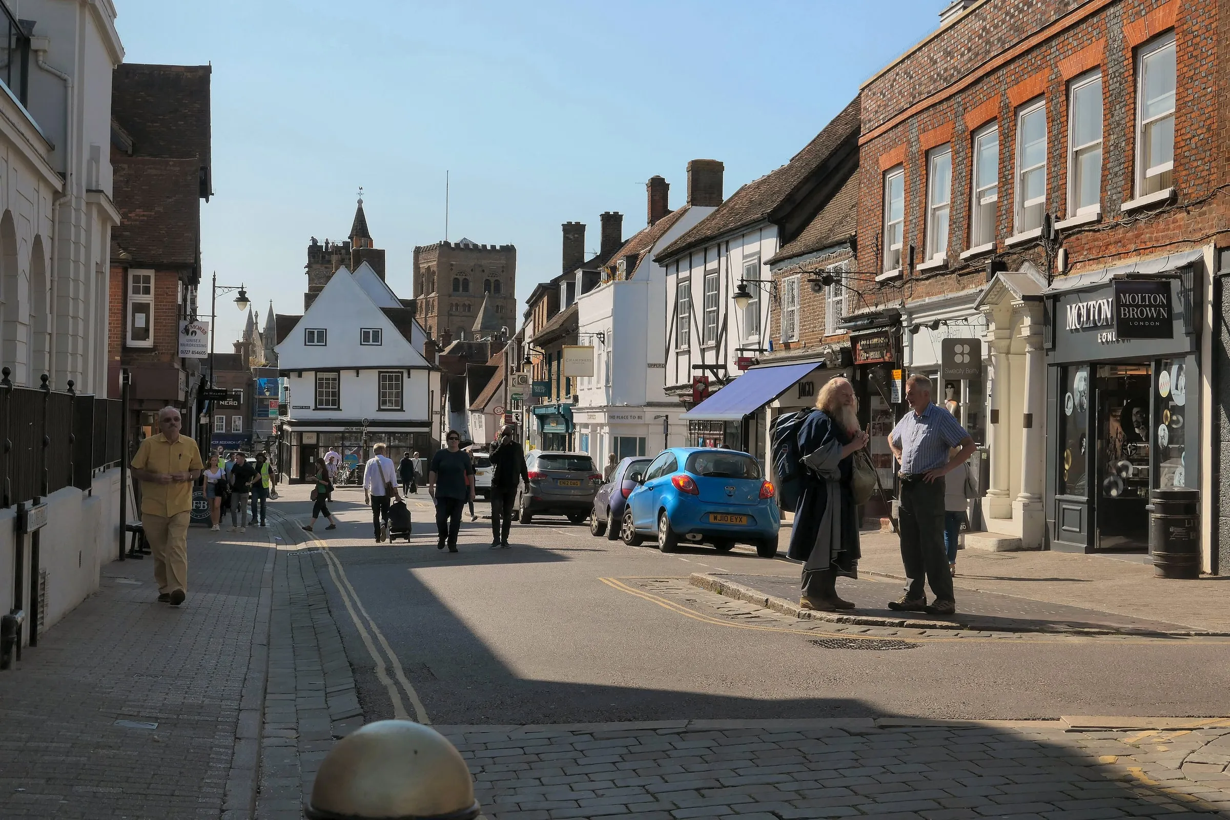 Shops and pedestrians along Market Place in St Albans city centre, with the clock tower in the distance